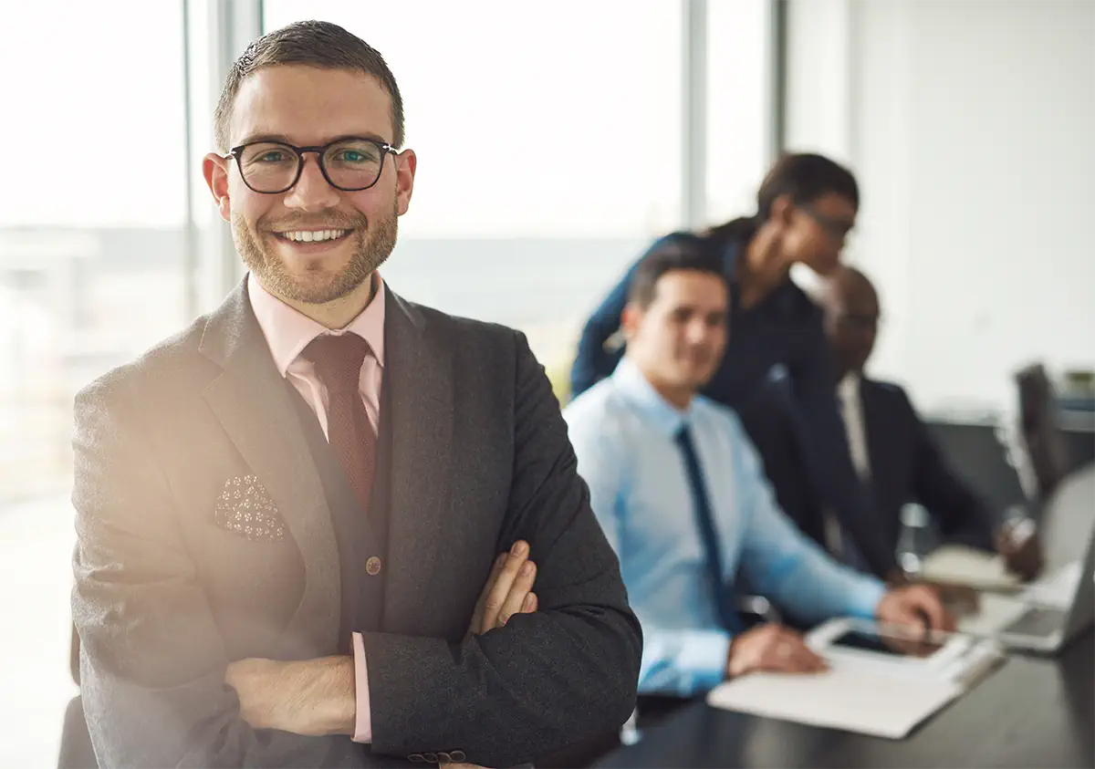 young business man standing and smiling with three coworkers behind him