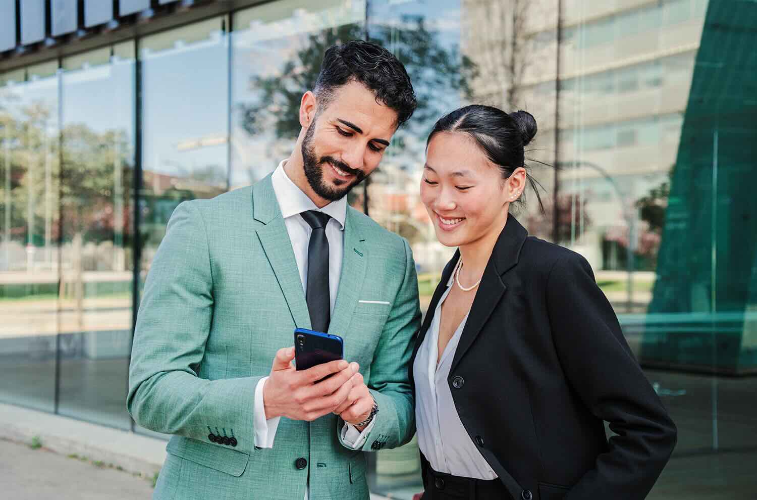 Two young businesspeople smiling and looking at a smart phone