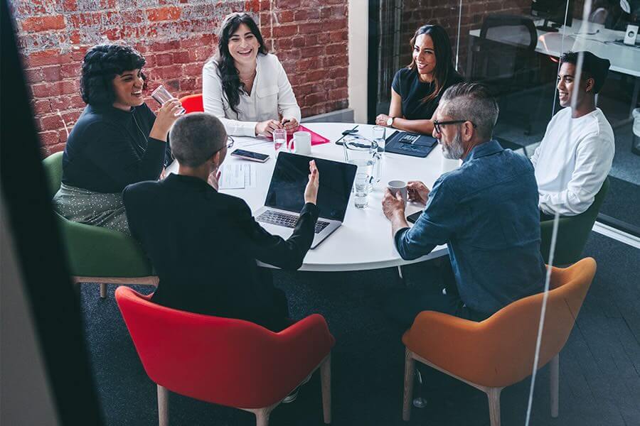 Six co-workers in a meeting speaking and sitting around a table